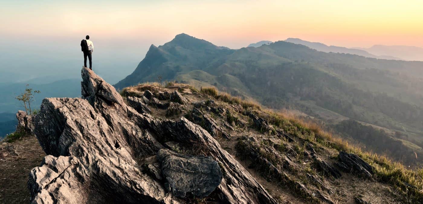 Businessman hike on the peak of rocks mountain at sunset