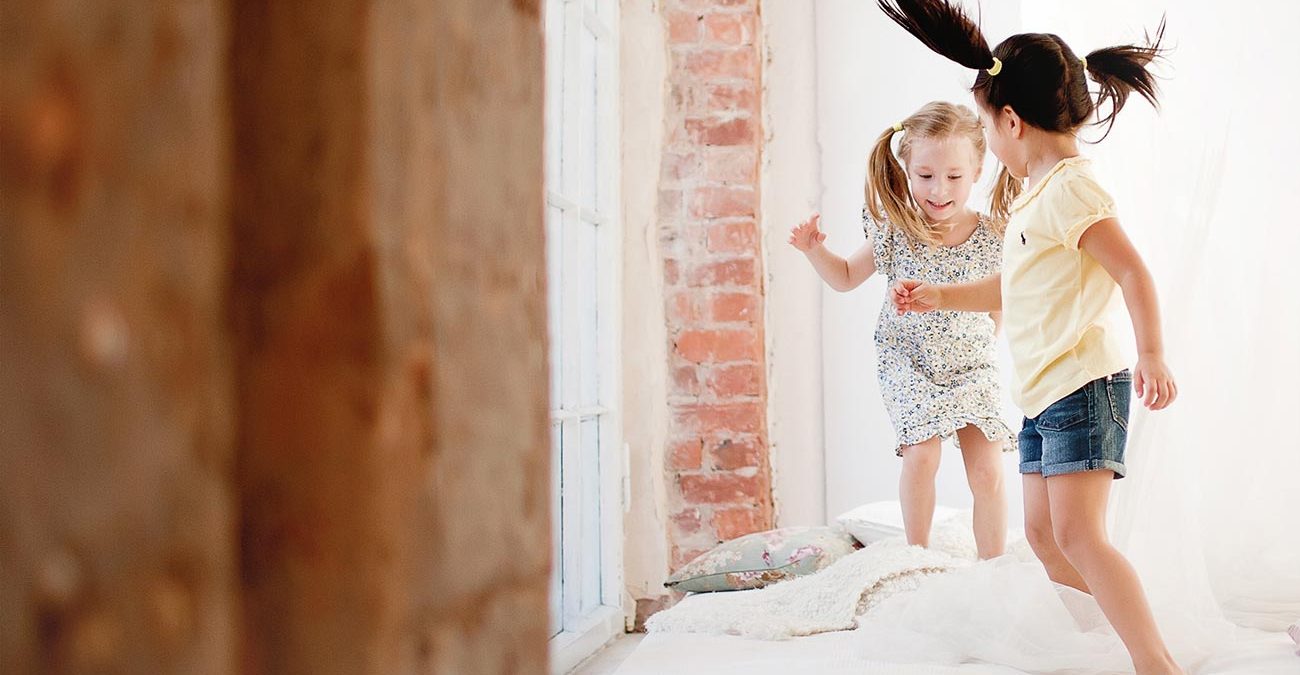 Two little girls are jumping on the bed