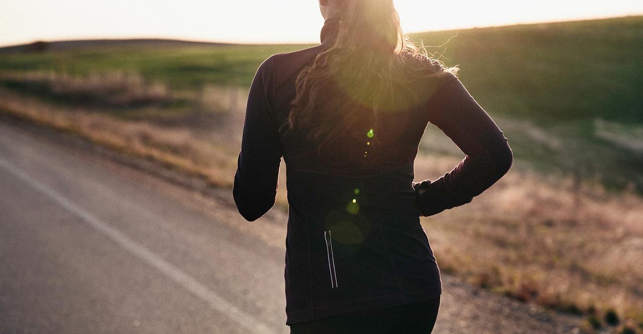 A woman running down a sunny road.