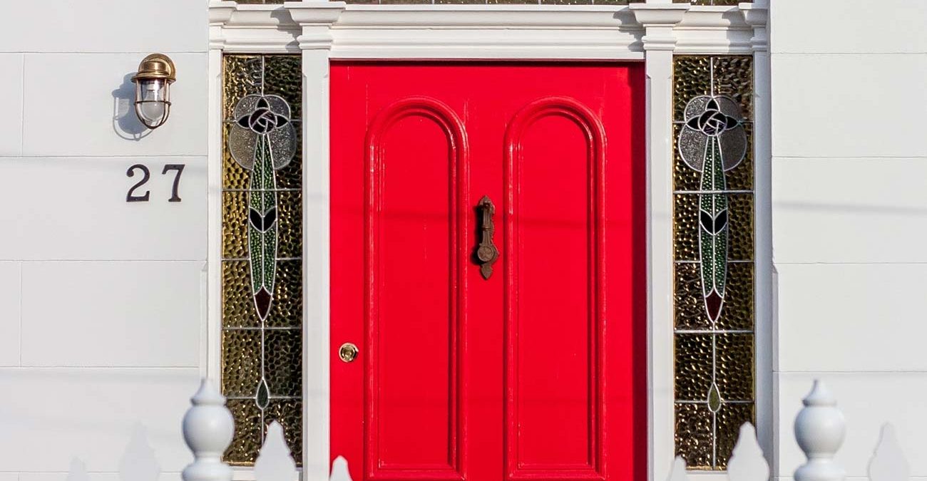 Red front door with white picket fence in urban streetscape