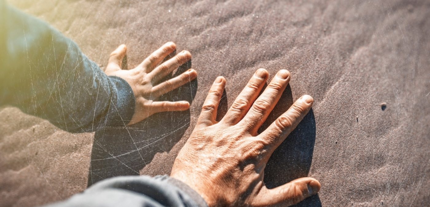 Child and grandparent's hand on the sand