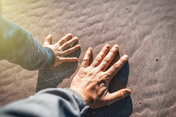 Child and grandparent's hand on the sand