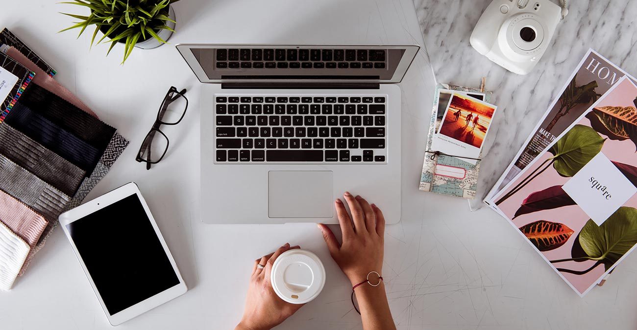 Flat lay of a clean and chic work desk: Ipad, Laptop, Camera, Magazines and Eyeglasses