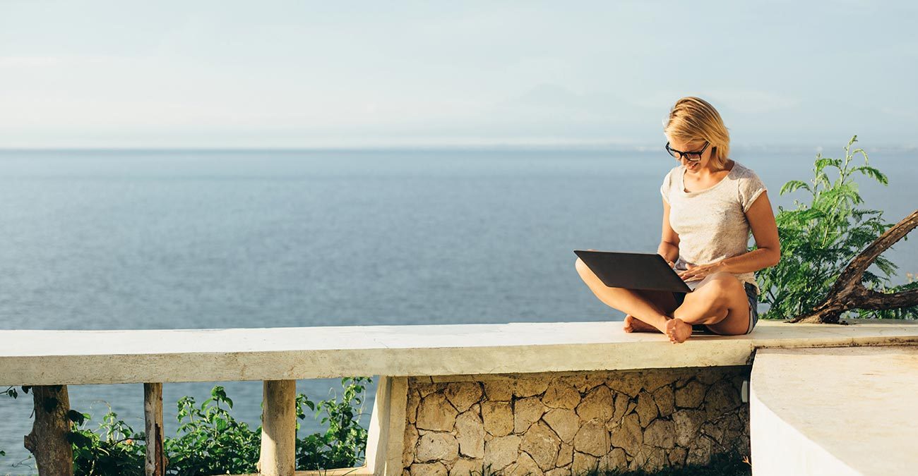 Blond girl working with a laptop on the tropical beach.