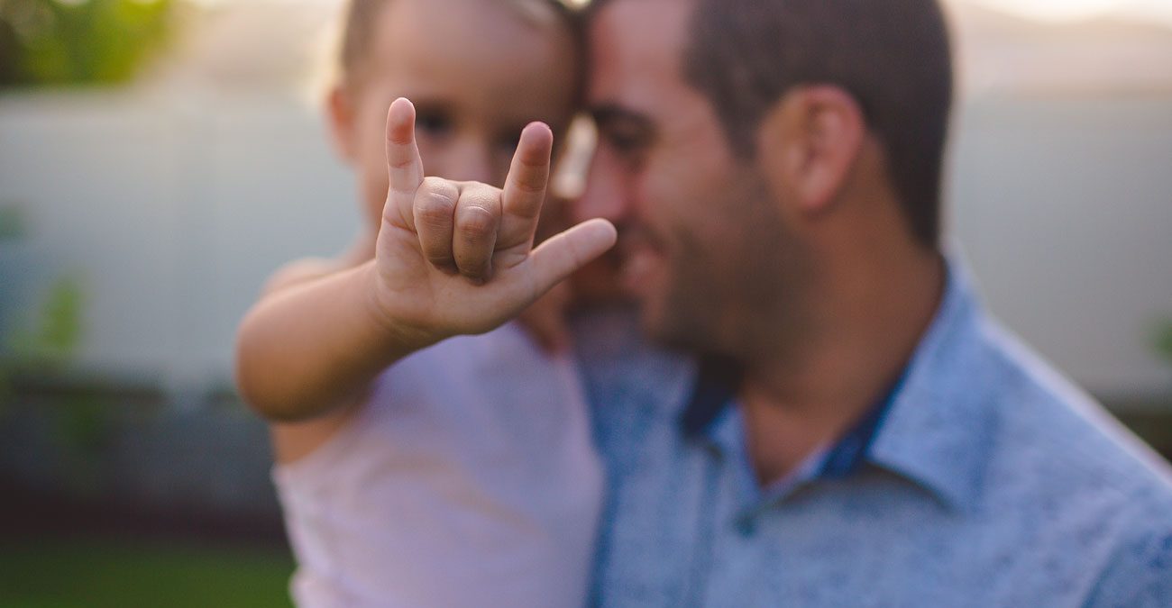 A dad with his young daughter doing the rock and roll sign.