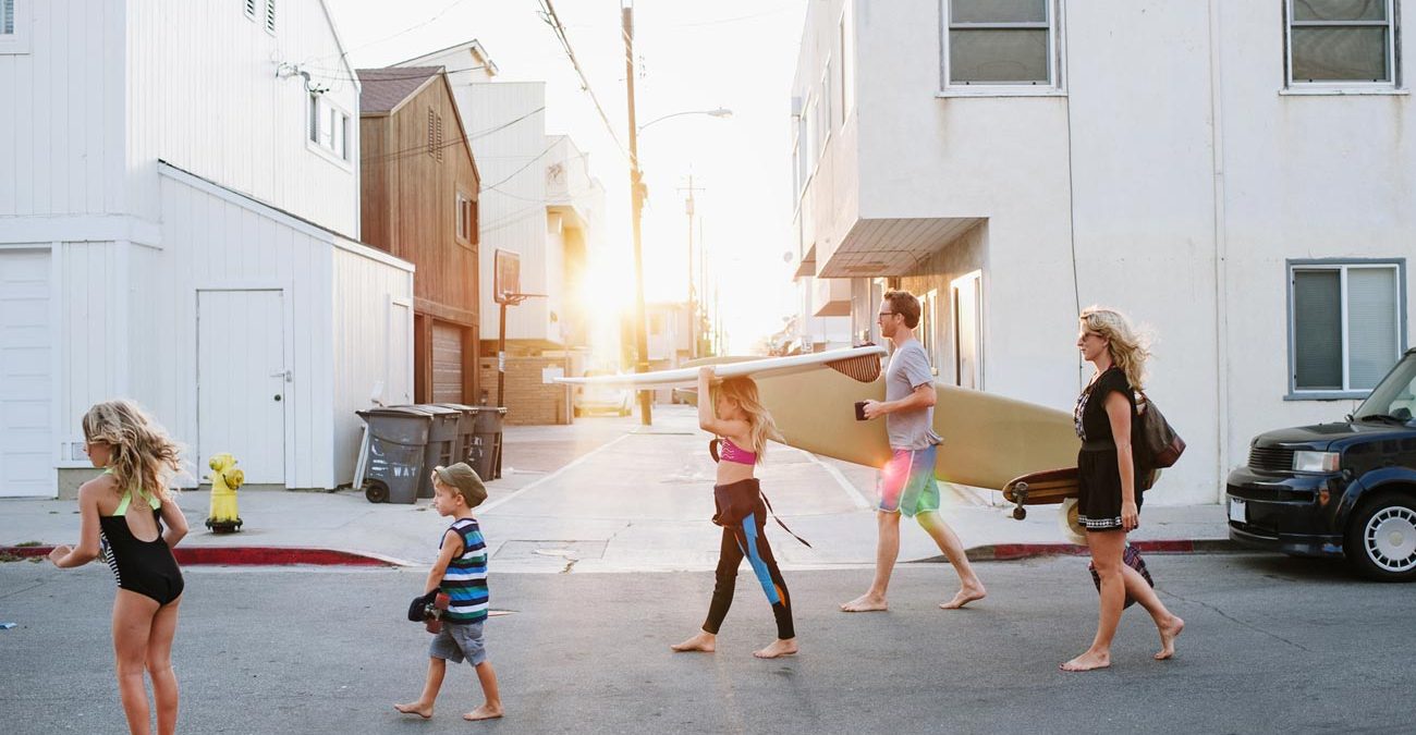 young family of five walking and skateboarding to beach through street