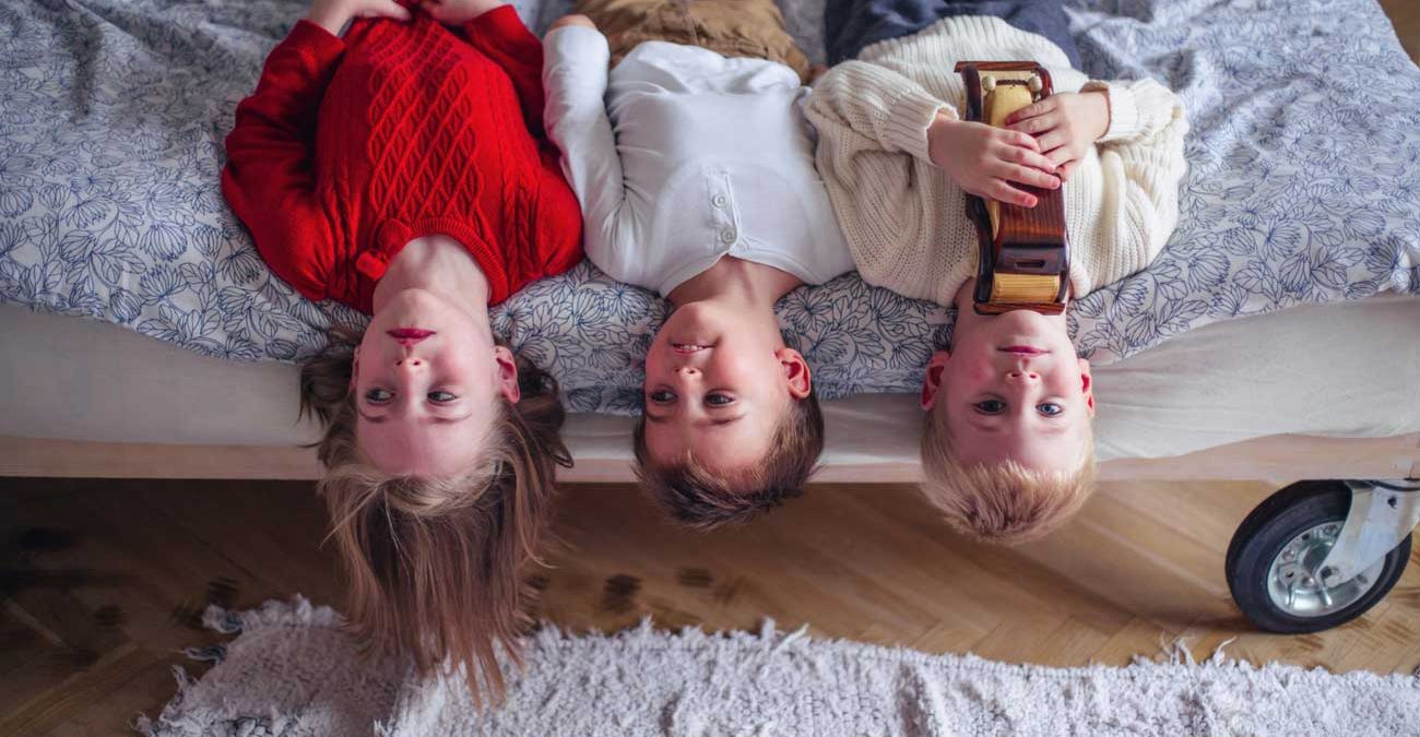 children laying upside down on the side of the bed